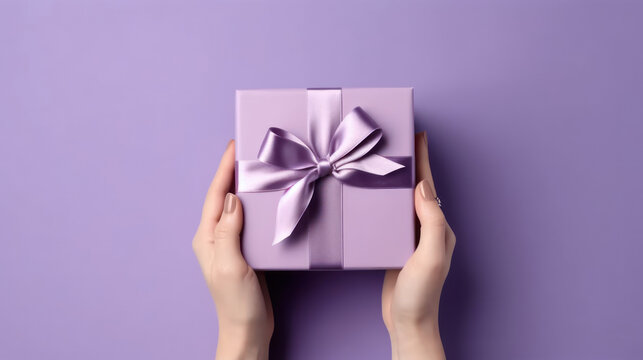 Female hands holding a purple gift box with a bow.