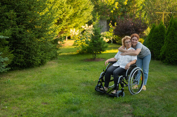 Caucasian woman hugging an elderly mother sitting in a wheelchair. Walk outdoors. 