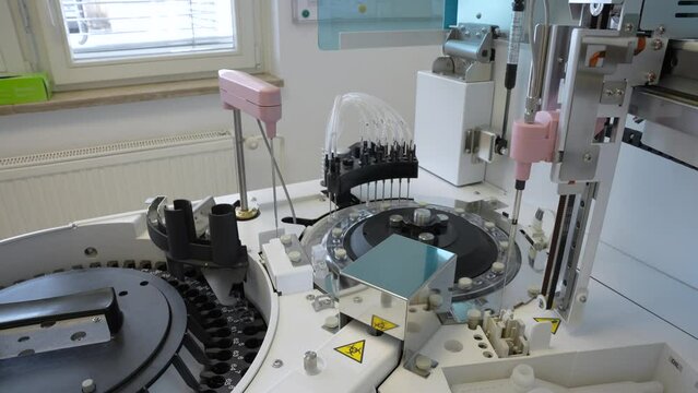 Small medical analyzer working on blood samples that are rotating on a disk in laboratory with a box of medical latex gloves in the background near the window