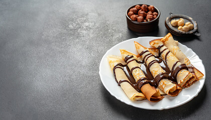 Pancakes with chocolate paste and hazelnuts, on a white plate on a background of concrete, slate...