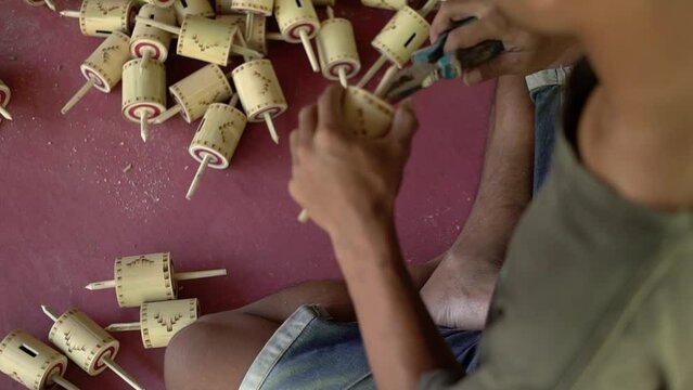 Details of making traditional Indonesian children's toys in the past, namely gangsing or tops made of bamboo and rope, which are done manually with simple tools by local craftsmen