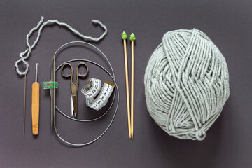 Accessories for hand knitting on dark gray background: skein of woolen yarn, scissors, measuring...