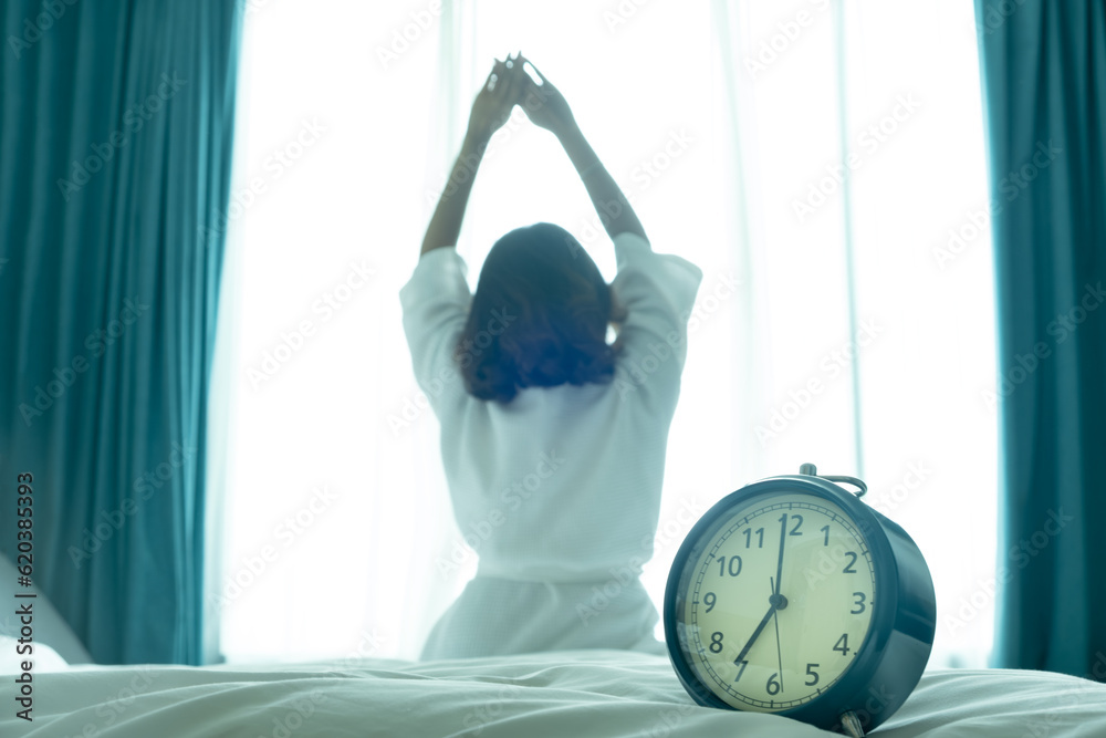 Wall mural Morning of a new day, alarm clock wake up woman sitting in the room. A woman stretch the muscles at window. Health and care concepts - Wall murals