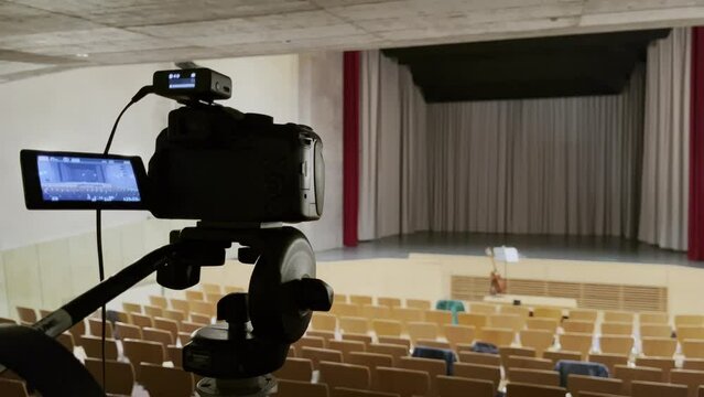 camera in an empty small concert steel with many chairs and empty stage on a tripod