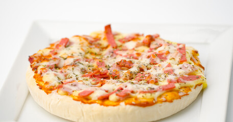 Hawaiian pizza is placed on a plate sitting on a white background.