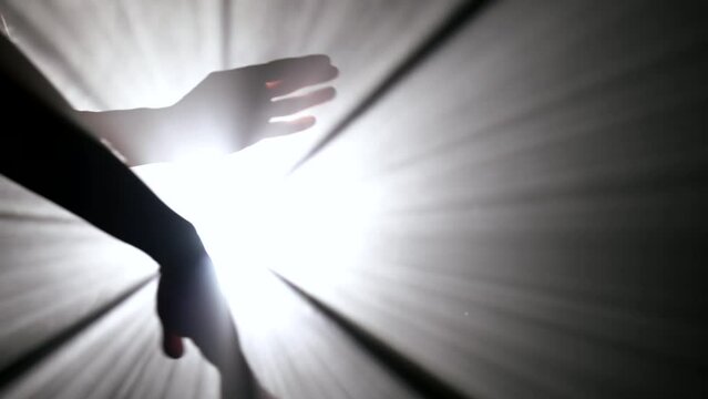 silhouette of female arms and hands moving slowly and sexually in darkness against bright soffit