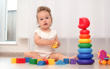 Charming kid is playing at home on floor with colorful cubes. Children's educational wooden toys. Concept of early childhood development