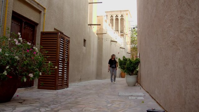 Al Fahidi is known for its Historical Neighborhood, with traditional buildings like 18th-century Al Fahidi Fort, now home to Dubai Museum's pearl-diving exhibits. Woman entering the historic place.