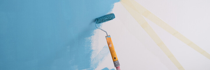 Decorator painting wall in blue color and using scotch tape and roller