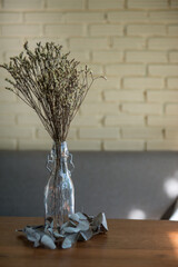 Dried flowers in a clear glass bottle, enhancing the decor on a wooden table with their rustic charm.