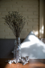 Dried flowers in a clear glass bottle, enhancing the decor on a wooden table with their rustic charm. - 620413337