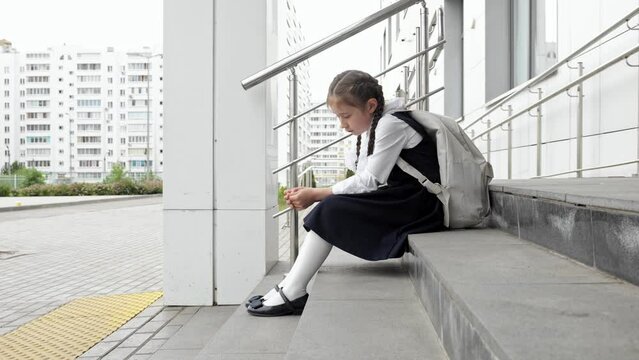 Junior schoolgirl sits with sad expression. Girl with long braids afraid to attend school and see bullies