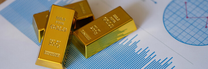 Small gold ingots on financial statistics document with charts and graphs