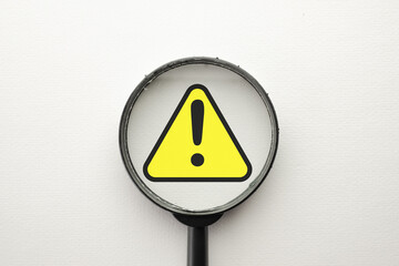 Magnify glass focus on Exclamation mark on a yellow sing or Warning sign over white background Attention sign,Exclamation mark,warning sign concept.