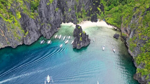 Bangka paraw canoes enter calm deep blue water bay and rocky cliffs