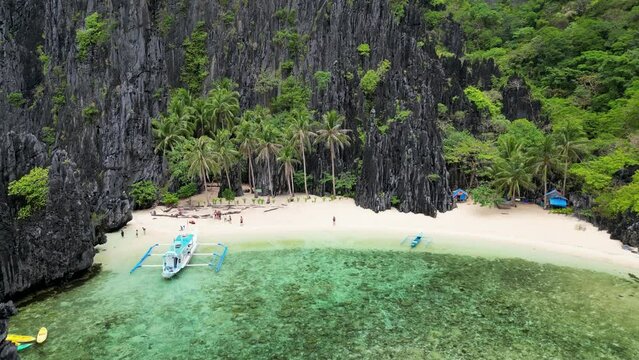 Peaceful sandy beach with paraw bangka boat and sheer rocky palawan cliffs