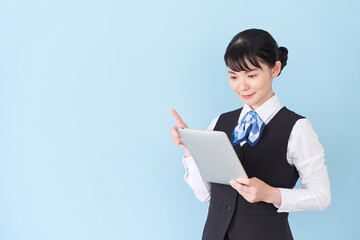 タブレットを操作するベストにリボンタイの制服を着た、受付業務、事務業務の女性