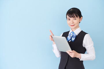 タブレットを操作するベストにリボンタイの制服を着た、受付業務、事務業務の女性