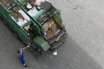 The garbage man working  on emptying dustbins for trash removal with truck loading waste and trash bin.