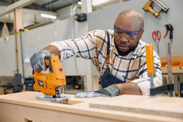 black african male carpenter joiner using Jig Saw wood panel cutter to cut making furniture panel in workshop