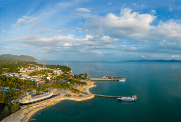 Naklejka na ściany i meble Ko Pha Ngan, Thailand: Aerial panorama of the Thong Sala ferry harbor and town in the Ko Phangan island in the gulf of Thailand with Ko Samui in the background.