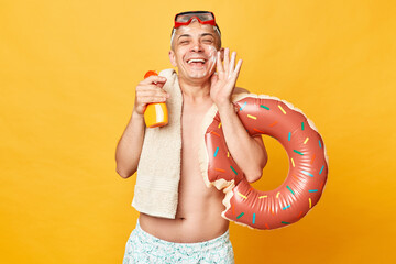 Delighted funny adult man wearing shorts swimsuit snorkeling goggles holding donut rubber ring and...