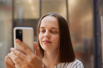 Closeup portrait of brown haired businesswoman using mobile phone looking at smartphone display with concentrated positive expression.