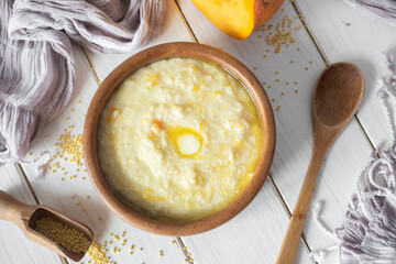 Delicious breakfast: millet porridge with pumpkin and a piece of butter in a wooden plate on a white background. View from above