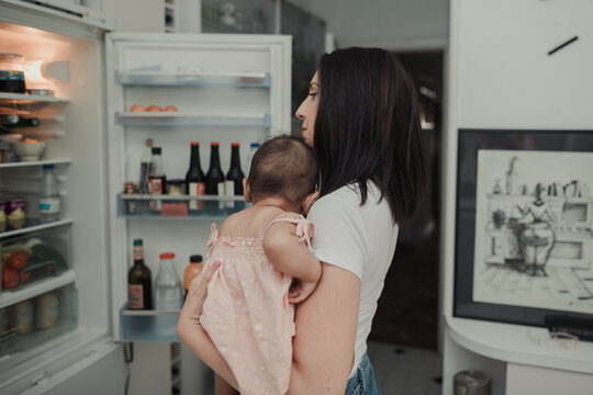 Woman looking into a fridge with a baby on hands