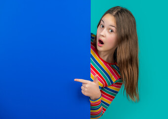 surprised girl behind blank blue paper with copy space for advertisement. point finger