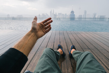 
View of the metropolis of Kuala Lumpur, from the roof of a skyscraper with a swimming pool, in the foreground the traveler's legs.