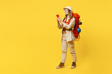Fototapeta na wymiar Full body side view young woman carry bag with stuff mat use mobile cell phone isolated on plain yellow background Tourist lead active lifestyle walk on spare time Hiking trek rest travel trip concept