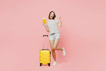 Full body traveler woman wear casual clothes t-shirt hold suitcase passport ticket isolated on plain pink background. Tourist travel abroad in free time rest getaway. Air flight trip journey concept.