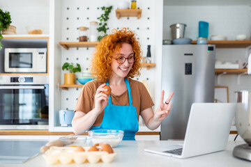 Obraz na płótnie Canvas A red-haired woman, following an online tutorial, bakes cookies in a modern kitchen. Tradition meets modernity as her skilled hands create delightful homemade treats in this stock image