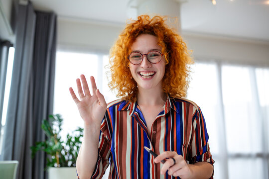 Businesswoman waves with enthusiasm on her video call. Her friendly gesture and warm smile bring a sense of connection and professionalism to virtual meetings, captured in this captivating stock image