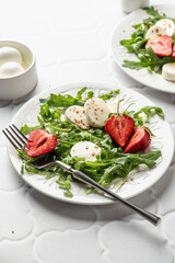 Salad with mozzarella with strawberries, mozzarella and arugula. Healthy light summer salad modern styling on white tile background text space
