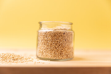 mixed raw quinoa in glass jar on rustic wooden table on yellow background