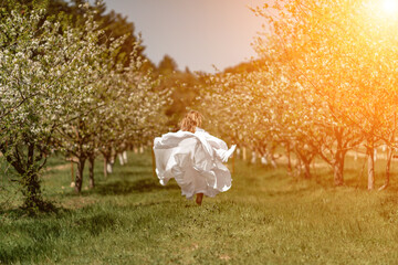 Woman white dress park. A woman in a white dress runs through a blossoming cherry orchard. The long...