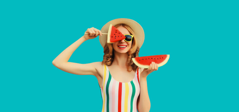 Summer portrait of happy smiling young woman with fresh juicy fruits, lollipop or ice cream shaped slice of watermelon wearing straw hat on blue background