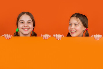cheerful children behind blank orange paper with copy space for advertisement
