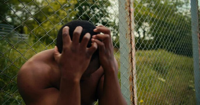 A man with a bare torso and Black skin is upset because he lost a basketball game. A man holds his hands on his head as a sign of his failure, he is upset and tired