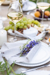 Romantic table decor for a loving couple on a meadow. Two glasses of wine, flowers in a vase, silverware, fruits, chandelier with burning candles, wooden furniture. Sunset, golden hour, summer