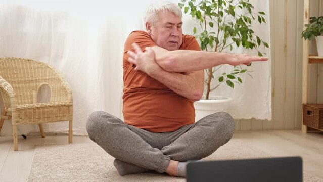 Happy smiling mature senior man doing exercises of gymnastics at home. Concept of healthy lifestyle, fitness, recreation, well being. Elderly male exercising training, stretching. Old man working out