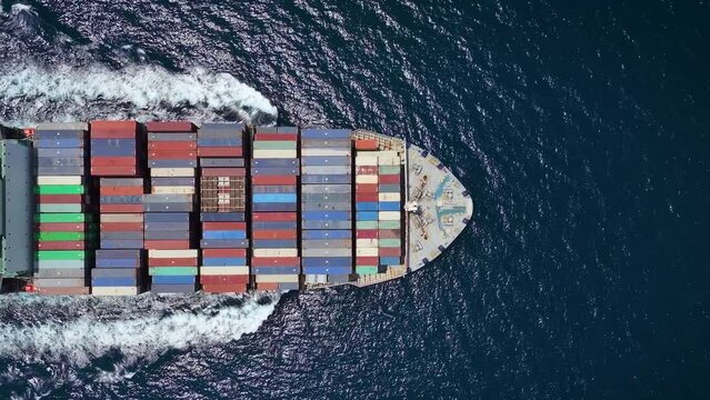 Aerial top down tracking of a large industrial container cargo ship crossing the sea with speed