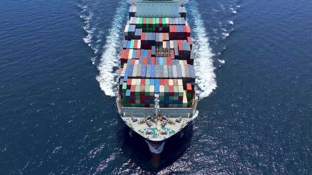 Aerial tracking of a large container cargo vessel traveling with speed over blue ocean