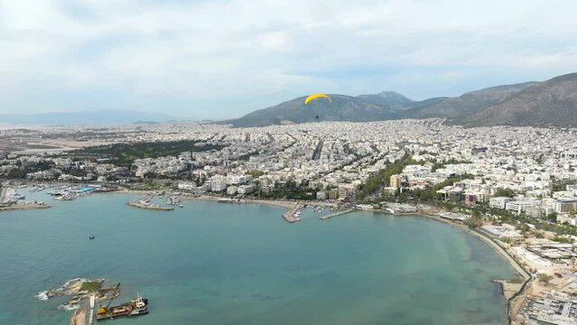 Yellow Powered Paraglider flyover turquoise waterbay in Glyfada cityscape, Athens. Greece