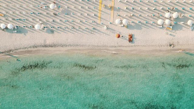 Vista aerea top-down della spiaggia in estate al tramonto con gli ombrelloni, il mare con acqua turchese cristallina  - Marina di Lizzano, Taranto, Puglia, Italy