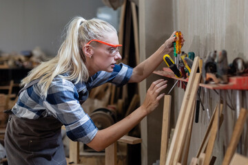 Woman carpenter wear uniform and goggles choosing a tool to use. craftsman profession in wood factory. female worker lathe working at manufacturing wooden industry.