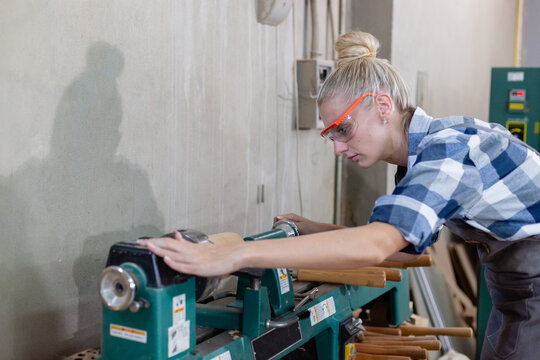Woman carpenter wear uniform and goggles using wood turning machine. craftsman profession in wood factory. female worker lathe working at manufacturing wooden industry.