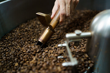 Professional coffee roaster working with modern automated roasting machine in the coffee roasting...